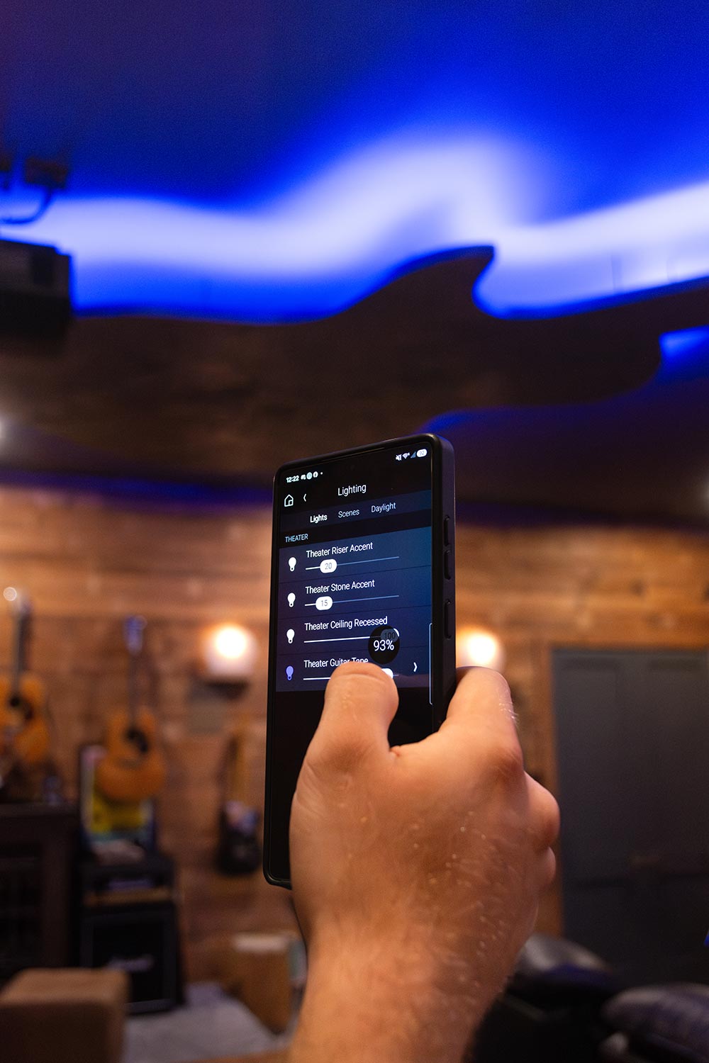 Hand holding smartphone showing lighting control app in a room