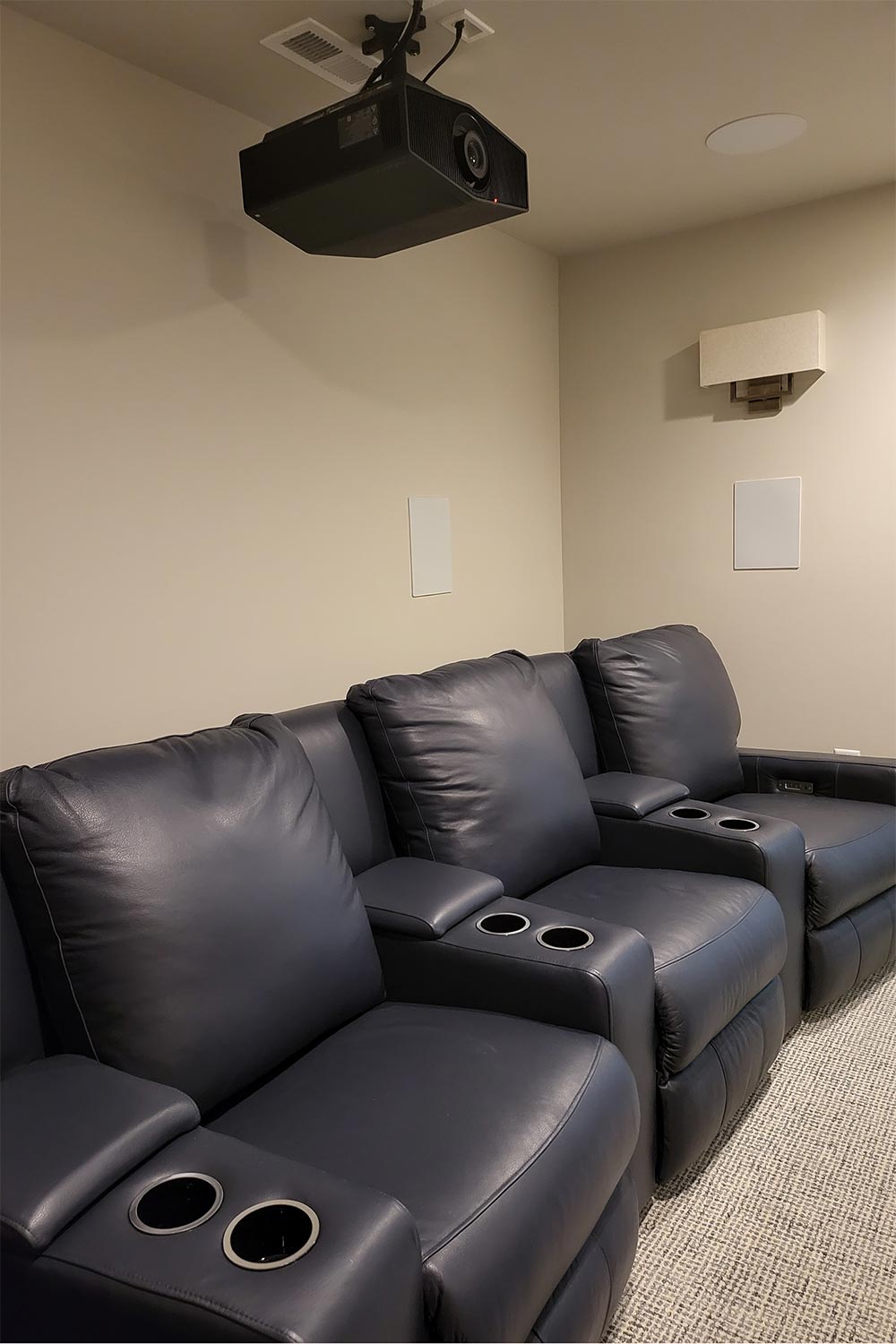 Three blue leather theater recliners under a ceiling projector