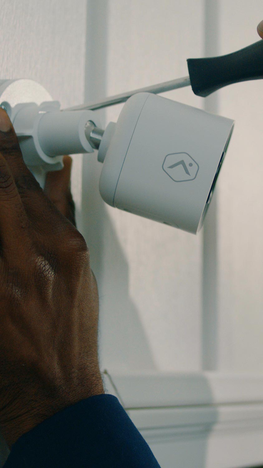 Person installing a white outdoor security camera with a screwdriver