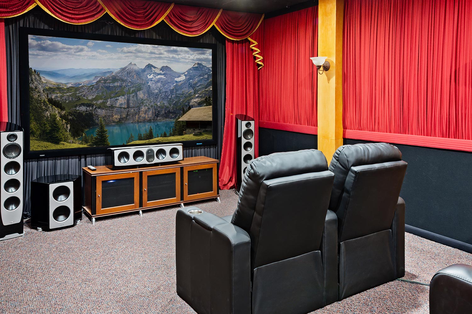 Home theater with large screen showing a mountain lake and black leather recliners