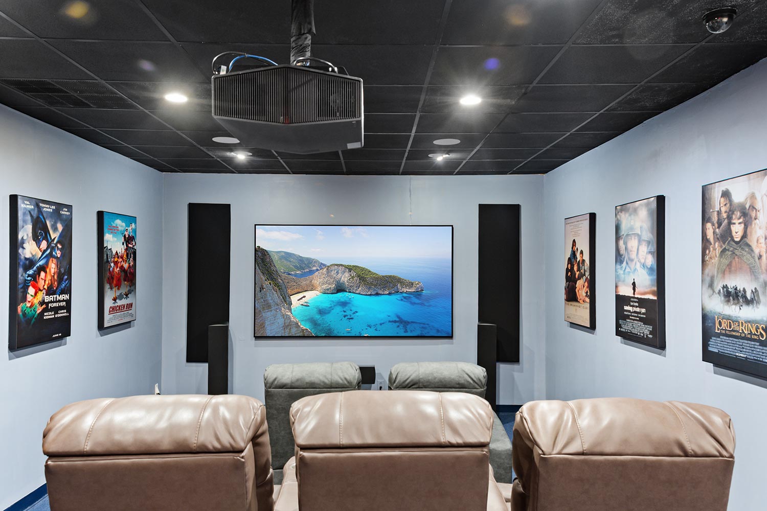 Home theater room with a projector screen showing a beach and framed movie posters