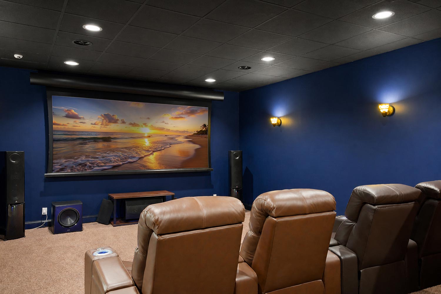 Home theater featuring brown leather seats and a large screen displaying a beach sunset