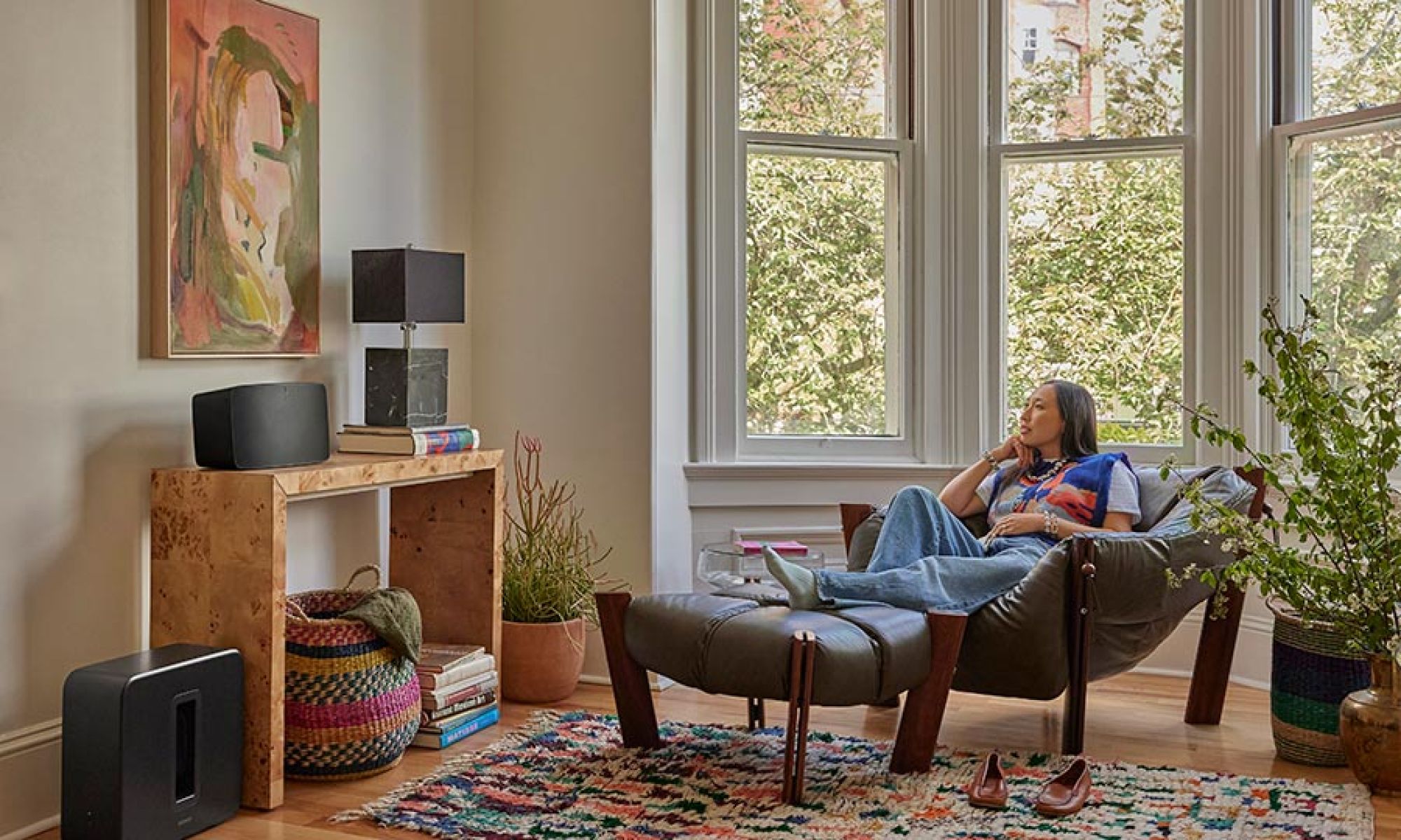 Woman relaxing in a chair near two black wireless speakers
