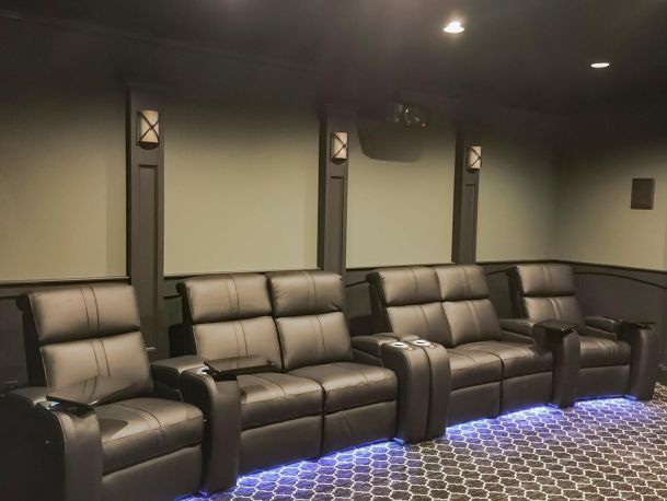 Four dark leather theater seats with blue LED underglow against green walls