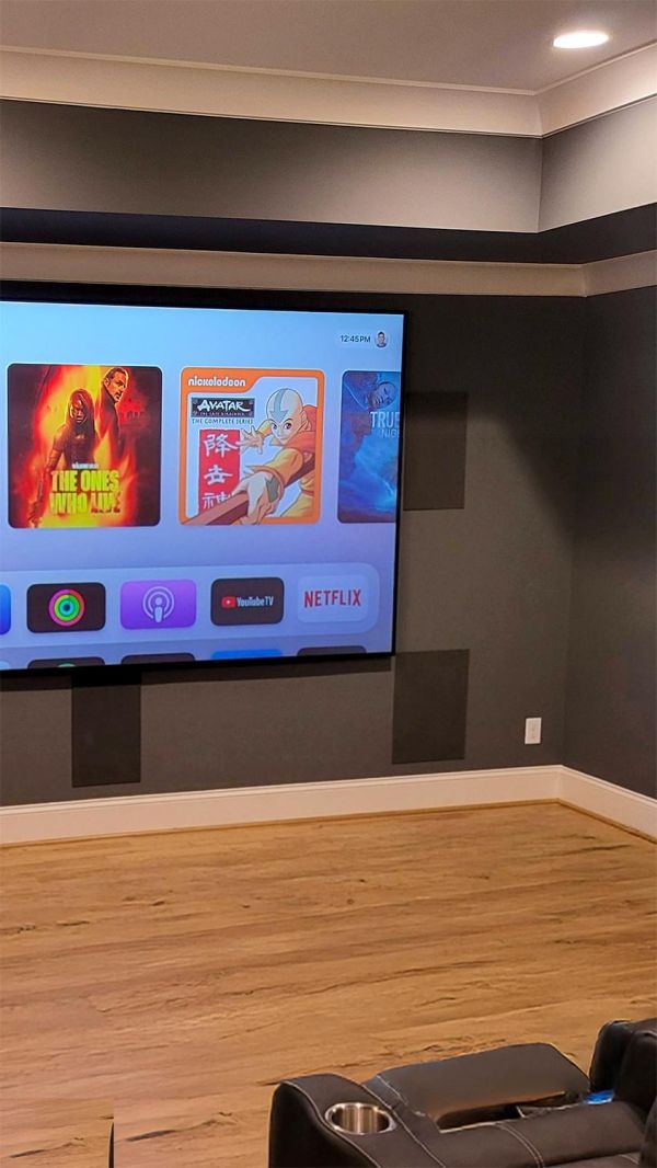 Large screen showing a media interface in a dark room with wood flooring and a leather seat