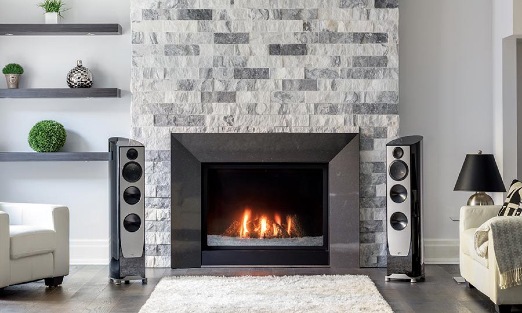 Two tall floorstanding speakers beside a modern stone fireplace