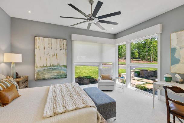 Bright bedroom with a bed large windows roller shades and a ceiling fan