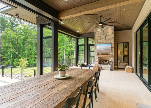 Covered outdoor patio with a wooden dining table stone fireplace and tv