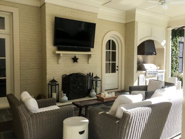 Covered outdoor patio with wicker seating and a television over a fireplace