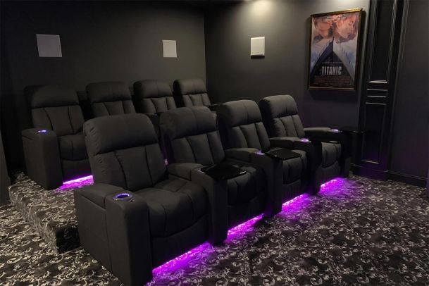 Two rows of black home theater recliners with purple underglow lighting