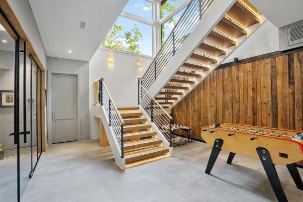 Modern wooden staircase with under-step LED lighting near a foosball table