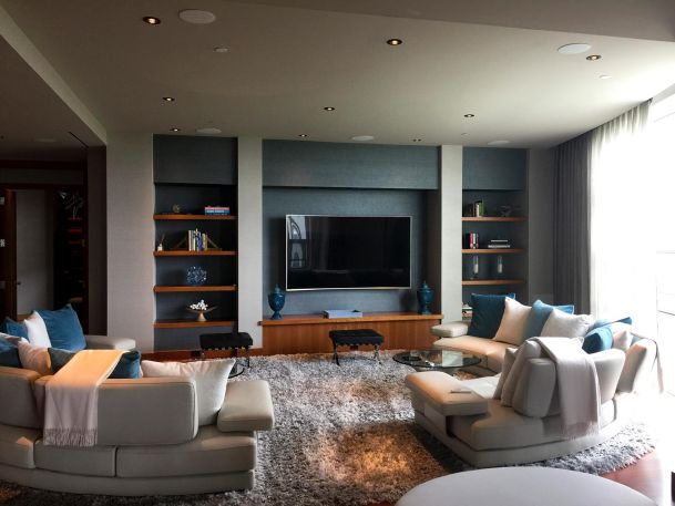 Living room with curved white sofas facing a large flat screen TV and shelves