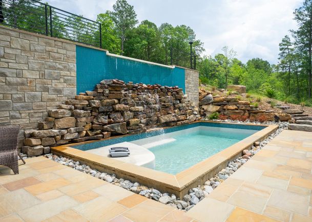 Small outdoor swimming pool with a rocky waterfall feature and stone patio