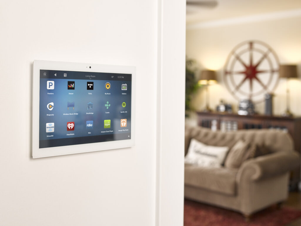 Wall-mounted smart home control panel next to a cozy living room.