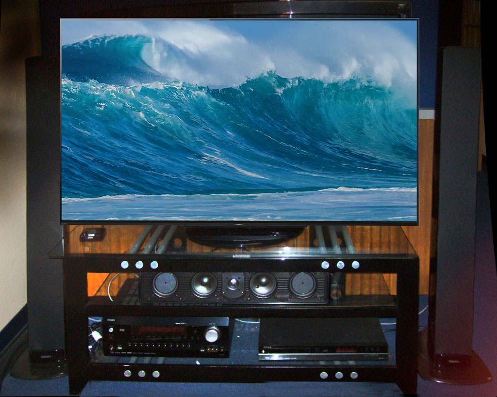 A large TV displaying a vivid ocean wave, placed on a wooden stand with audio equipment.